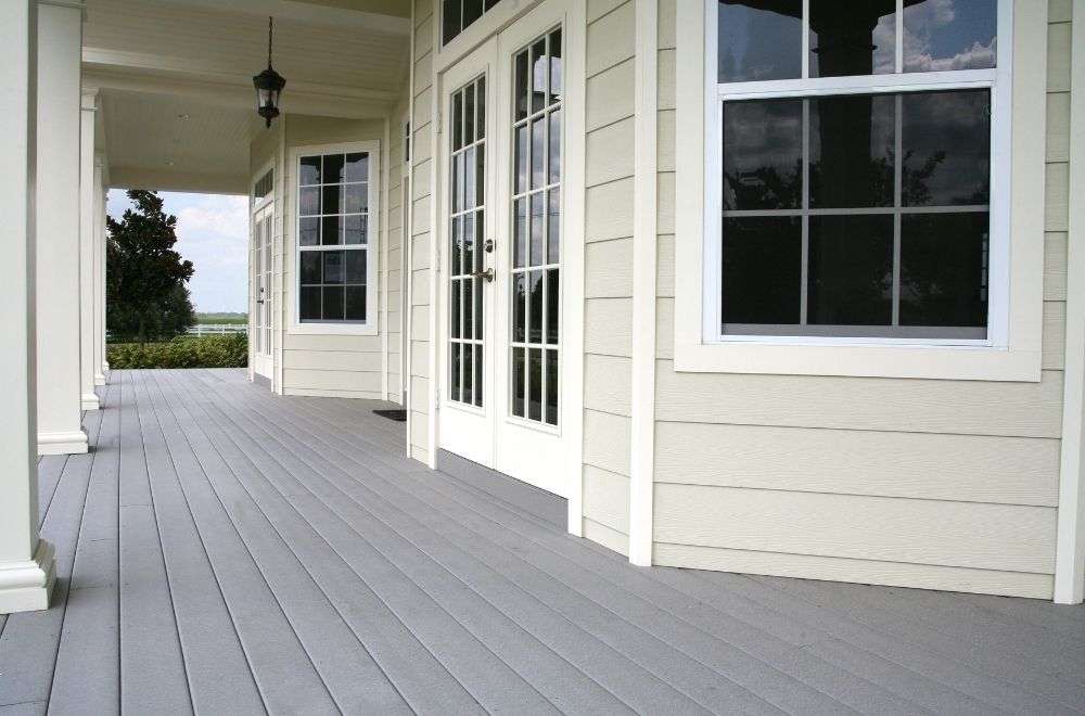 A house's expansive porch with grey decking, large windows, French doors, and a clear view of the sky.