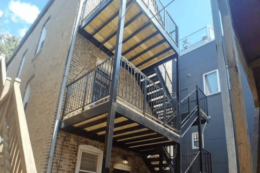 Metal staircases and balconies on the exterior of a brick building with a clear sky above. ( our Services )