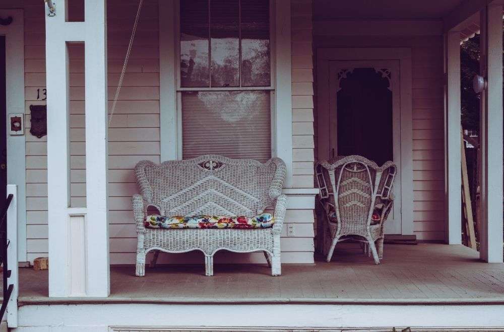 A cozy porch with a wicker loveseat and chair, swing, white columns, and the number 13 by the door.-A History Of Porch Violations