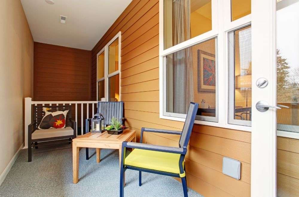 A bright enclosed porch with wooden walls, a bench with a star cushion, a blue chair, a wooden table, and a potted plant.-Importance Of Porch Maintenance