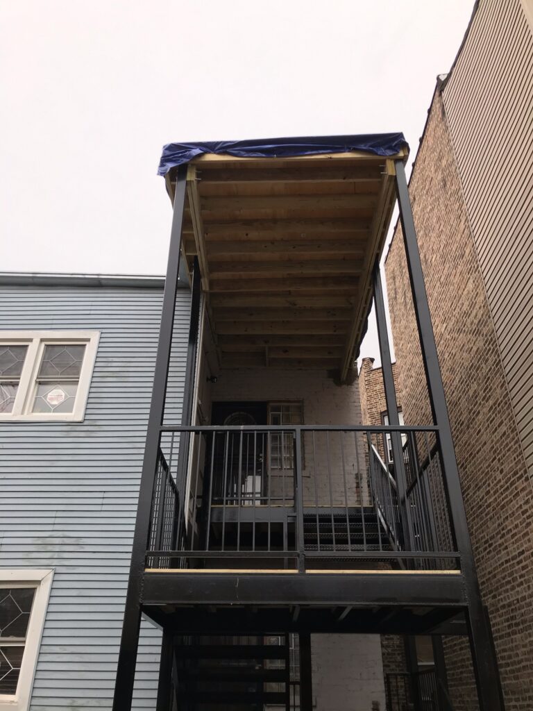 Free Estimates For Porches: Black metal staircase leading to a wooden deck with blue tarp overhead.