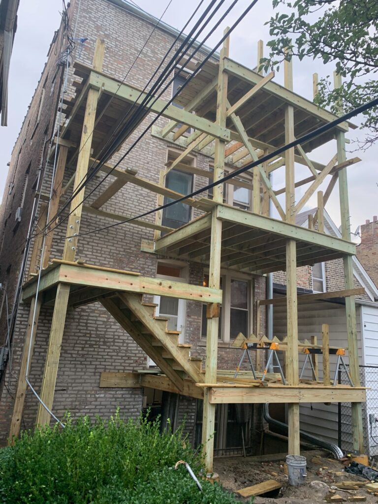 Construction of a multi-level wooden porch framework on the back of a brick building. ( Free Porch Inspection )