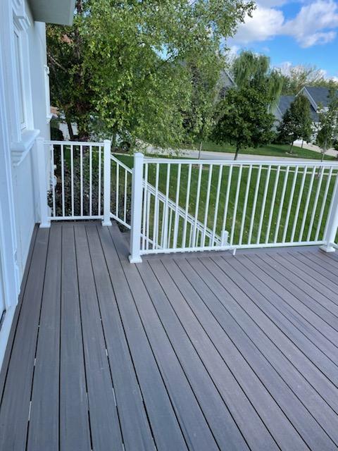 Grey composite decking with white railing on a residential porch surrounded by lush greenery.