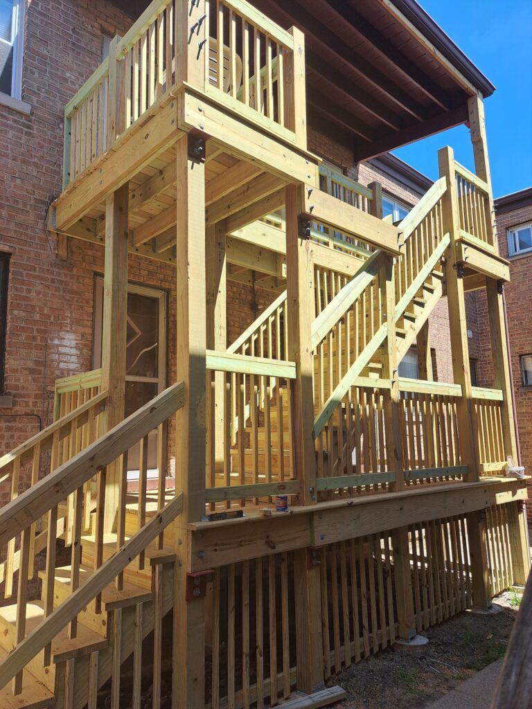 A newly constructed wooden railing height chicago and landing on the exterior of a brick building with bright sunlight.