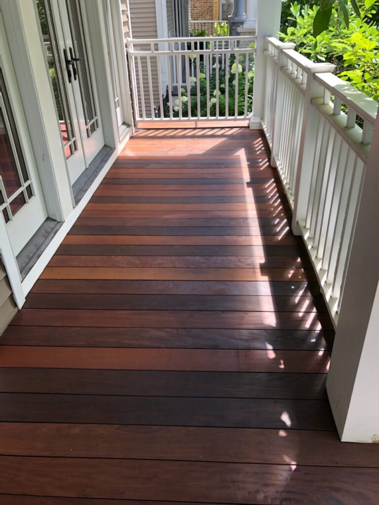 Trex decking on a home's porch, featuring a deep wood tone with white railing and surrounded by greenery.