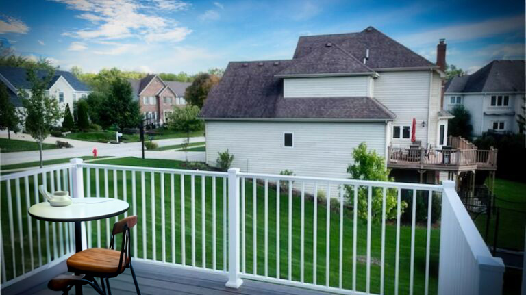 A balcony view with a small table and chair overlooking a lush suburban neighborhood with well-kept homes and lawns.