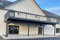 Elevated black balcony with railing on a white brick building facade.