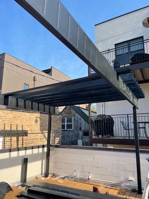 Metal deck framework with beam a staircase and balcony against urban buildings under a clear blue sky.