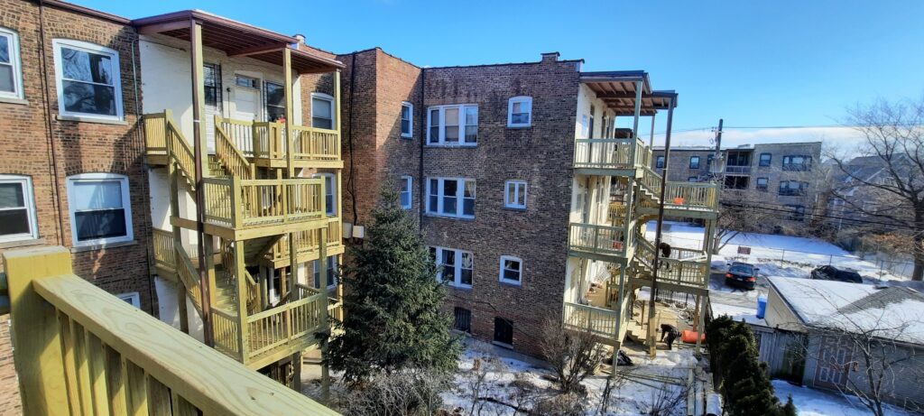 Apartment building with wooden balconies and staircases against a winter backdrop.-ground line