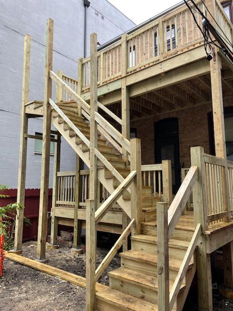 A new wooden staircase and deck structure on the exterior of a two-story building with beige walls.