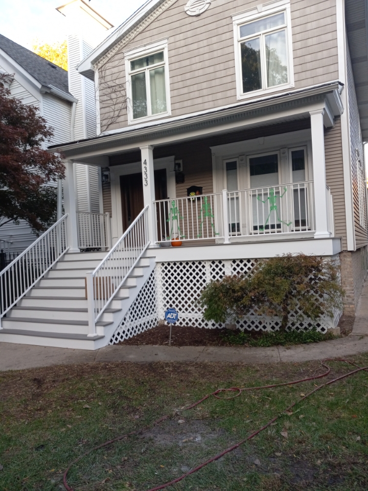 Residential two-story house with gray siding, featuring a white front porch with composite Deck, stairs, railings, and lattice skirt beneath.