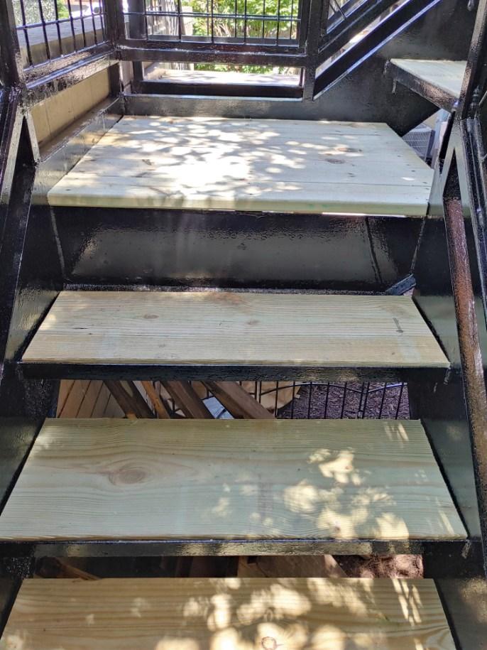 Looking down a set of outdoor wooden steps with a metal handrail, dappled with sunlight filtering through leaves.-STAIR STRINGER