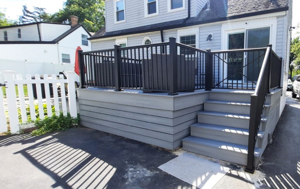 A steel deck with black railing and matching steps leading to a house with white siding, under a clear sky.