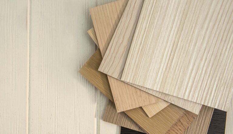 A selection of wooden vinyl tiles in various shades fanned out on a light wooden floor.