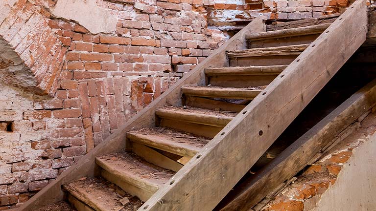 Weathered wooden staircase against a crumbling brick wall.