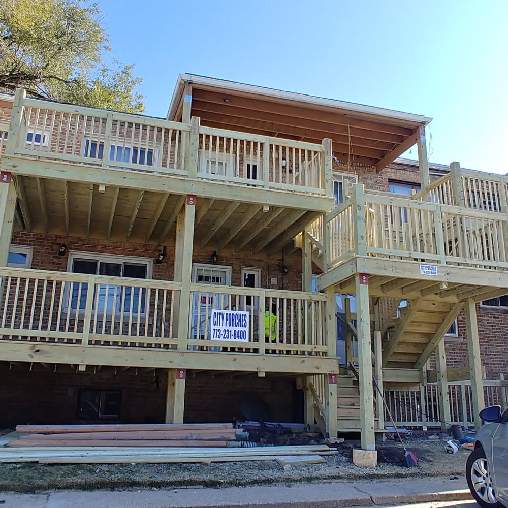 A new wooden porch construction on a brick building with multiple levels, featuring a banner with contact details