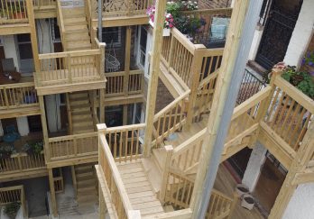 photo_1 An overhead view of a wooden fire escape with multiple staircases connecting various levels of an apartment complex. ( city Porches )